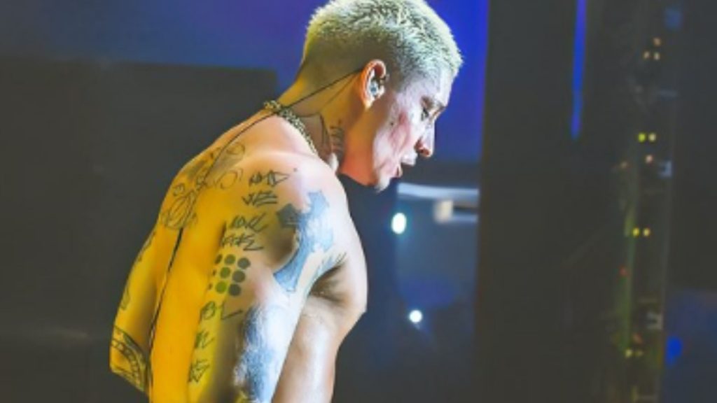 Cantor de rap Filipe Ret durante show em Recife. Ele está com o olhar direcionado para baixo e sem camisa. As tatuagens do braço e costas estão em evidências. 