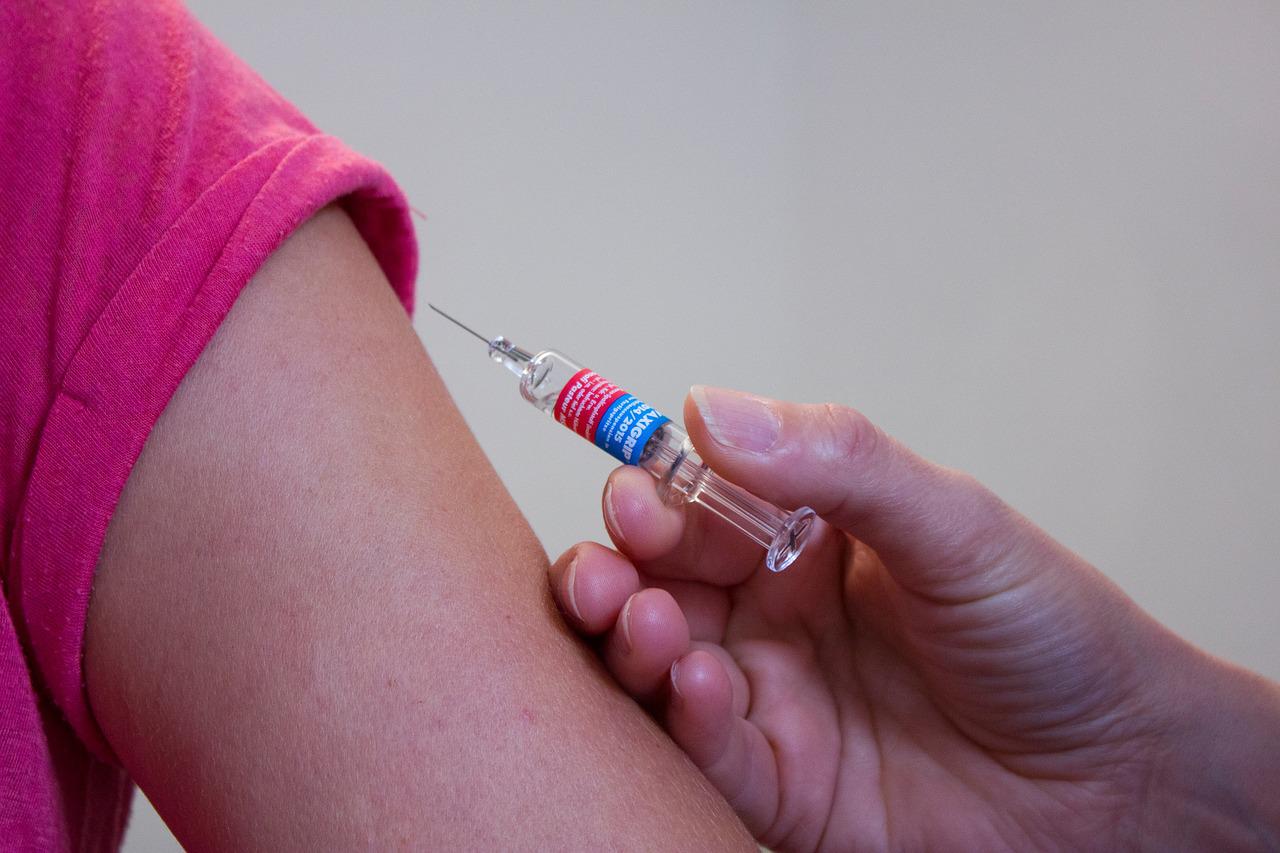 Braço prestes a receber uma vacina na agulha. Uma mão está segurando a seringa.