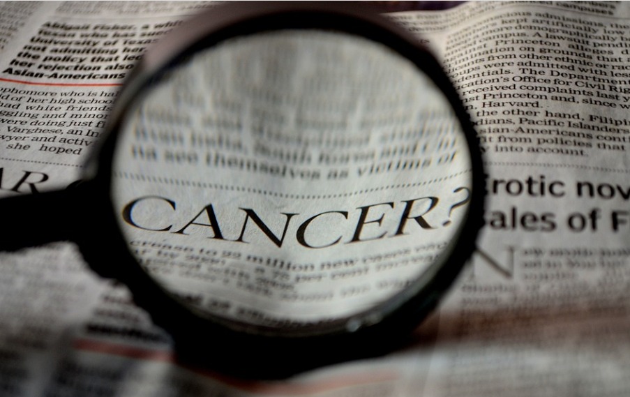 Folha de um jornal com uma lupa focada na palavra Cancer.